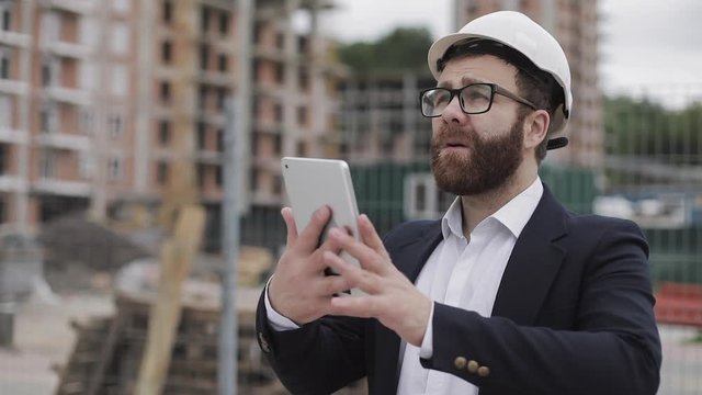Young bearded architect at the construction site taking photo with tablet. He dressed in business suit.