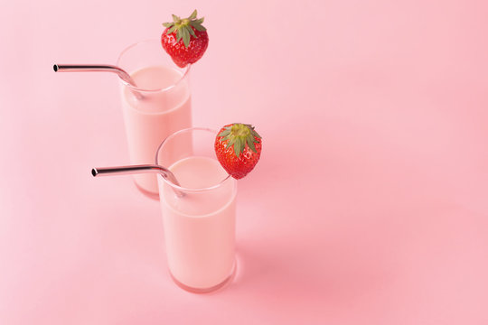 Two glasses with strawberry milk on pink background