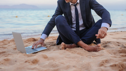 close up photo of a young man in suit with laptop working on the beach and talking to someone