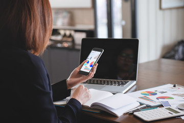 Business people are holding a smartphone and use it to check information at hand ,Businesswomen work in office using a laptop computer, job analysis and job description checking