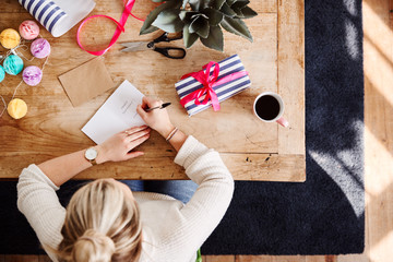 Overhead Shot Looking Down On Woman At Home Writing In Birthday Card And Wrapping Gift