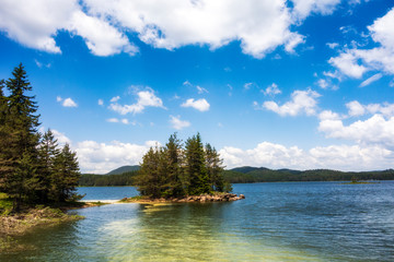 Summer time in the mountain, beautiful lake and green forest with blue sky and white puffy clouds