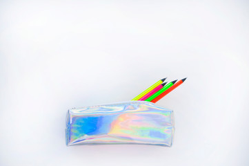 Colorful paper, neon pencils and holographic pencil case on beige background with copyspace. Flat...