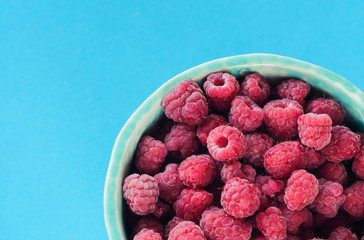 Top view on ripe fresh isolated raspberry bowl on the blue background