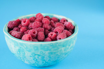 Close up view on ripe fresh raspberry bowl on the blue background