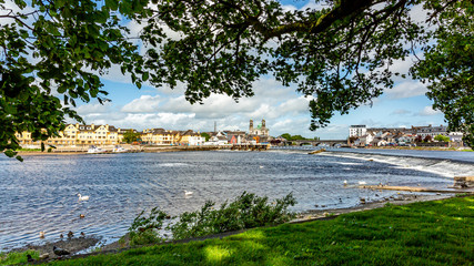 River Shannon with flowing water seen through branches with green foliage of a tree with Athlone...