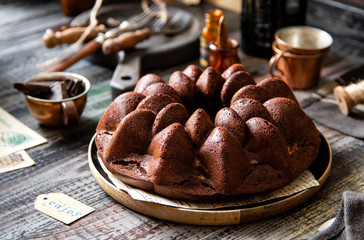 Delicious homemade chocolate bundt cake on wooden plate stands on rustic table