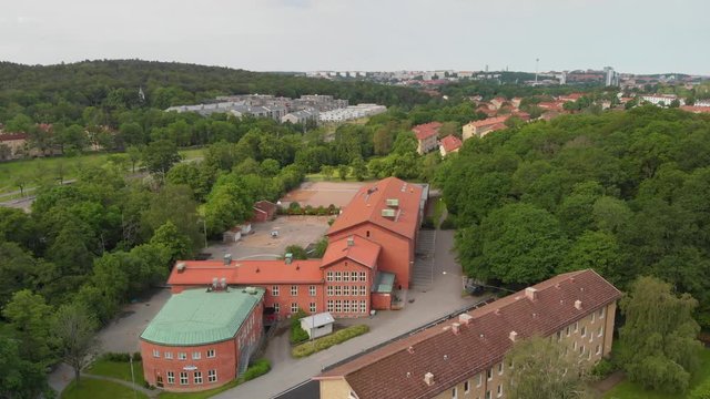 Aerial video of Karralundsskolan, school, in the suburb Orgryte torp in Gothenburg, Sweden, showing the building and the schoolyard and lots of lush green trees and bushes around it