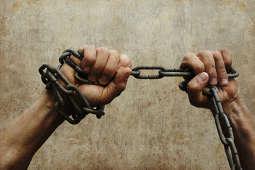 photo with grunge processing, where men's hands wrapped in a large iron chain try to break them, the concept of bondage, struggle, save space, close-up