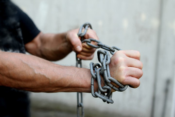 men's hands wrapped in a large iron chain, trying to break them, the concept of bondage, struggle, save space, close-up