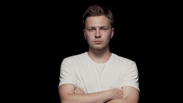 Serious caucasian male looking at camera with arms folded. Black bg, white t-shirt.