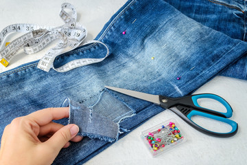 Woman hand shows a large hole on pant leg of a blue jeans folded in half. Jeans are prepared for...