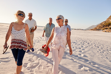 Group Of Senior Friends Walking Along Sandy Beach On Summer Group Vacation