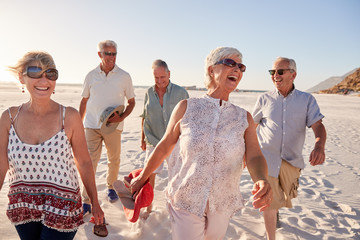 Group Of Senior Friends Walking Along Sandy Beach On Summer Group Vacation