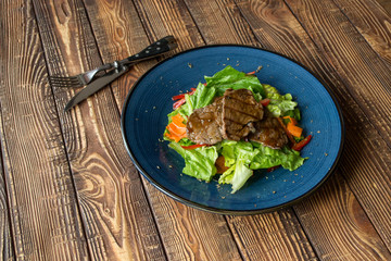 The hot salad with meat on a wooden background.