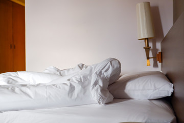 White crumpled bed sheet and messy pillows in a hotel room
