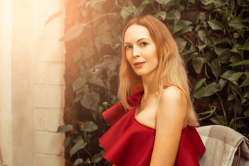 A beautiful young woman in an asymmetrical red-burgundy cocktail dress on one shoulder sits in a...
