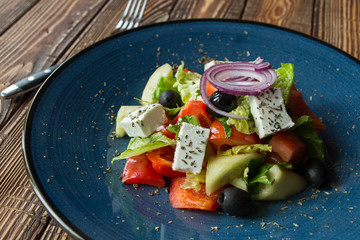 Greek salad in a plate on a wooden table.