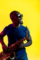 Young african-american jazz musician playing the saxophone on yellow studio background in trendy...