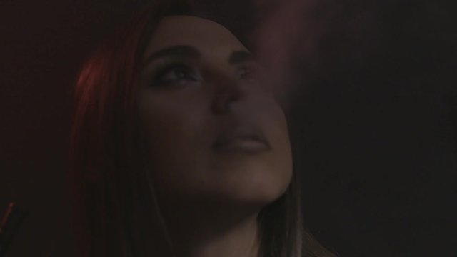 Beautiful sexy brunette girl with bright makeup exhaling smoke from her mouth on black background, bad habits concept. Action. Portrait of young woman smoking hookah.