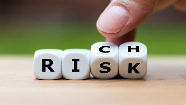 Take a risk and getting rich concept. Hand turns dice and changes the word "RISK" to "RICH".
