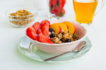 Healthy vegetarian breakfast. A bowl of granola, berries and fruit. In the background a glass of green tea and strawberries on a white background. The concept of healthy eating, diet
