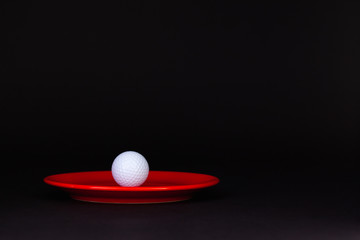 Red plate and golf ball on the black table