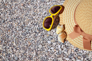 Hat, shells and sunglasses on a pebble beach.