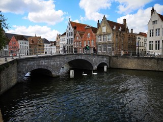 Walkers on a bridge, swans on a canal and Bruges architecture in the background