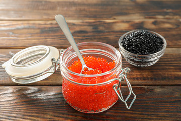 Glass jars with caviar on wooden table, space for text