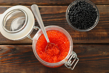 Glass jars with caviar on wooden table, space for text