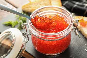 Composition with caviar in glass jar, bread, spoon, towel and cutting board, space for text