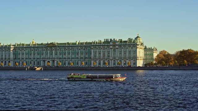 A boat floating left to right on Neva river on background of Winter Palace in Saint Petersburg in spring. Calm weather and clear blue sky with no clouds