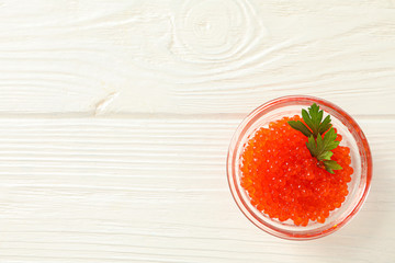Glass jar with red caviar isolated on white wooden table, space for text