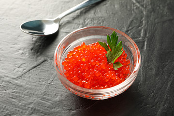 Glass jar with caviar and spoon on black background, space for text