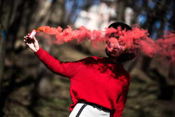 Young pretty woman holding red colorful smoke bomb on the outdoor park. Red smoke spreading in the cerebration festival. - Powered by Adobe