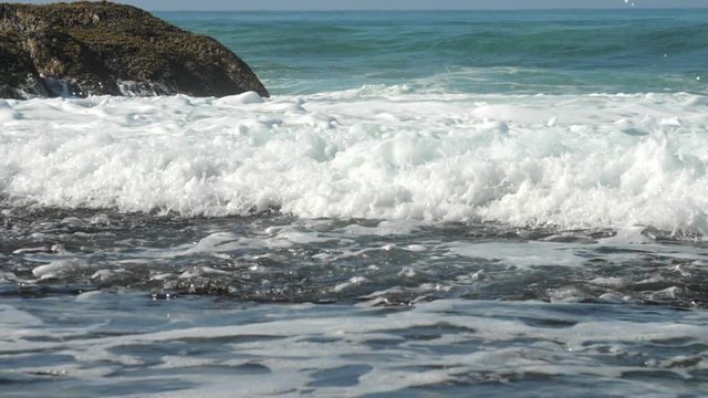 beautiful ocean waves foam near brown rock against blue endless water slow motion. Concept endulf low-lying areas and global warming