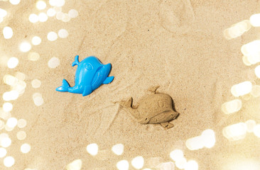Fototapeta na wymiar toys, childhood and vacation concept - sand shape made by whale mold on summer beach