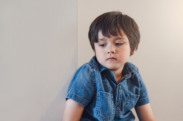 Emotional portrait of Unhappy boy sitting next to wall with sad face, Upset kid sitting alone and...