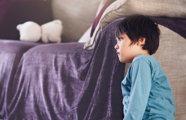 Emotional protrait of Sad boy wearing pyjamas sitting next to the sofa in the morning, Lonely kid...