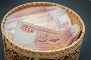 A lot of banknotes worth five thousand rubles are in a round wooden wicker box.