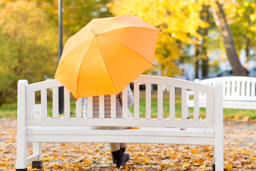 season, rainy weather and people concept - woman with umbrella sitting on bench in autumn park