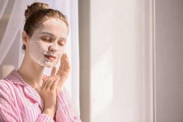 Young woman with sheet facial mask at home