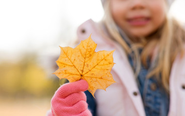 childhood, season and nature concept - close up of little girl with maple leaf in autumn