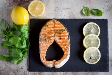 Salmon steak on a platter with slices of lemon.