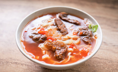 Beef noodle ramen meal with tomato sauce broth in bowl on bright wooden table, famous chinese style food in Taiwan, close up, top view, copy space