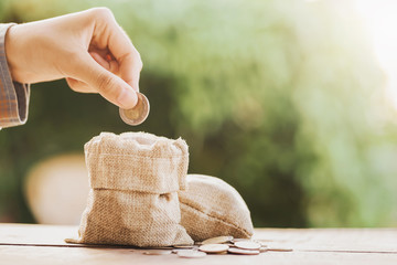 hand puting coins in money bag for saving on table background
