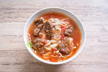 Beef noodle ramen meal with tomato sauce broth in bowl on bright wooden table, famous chinese style food in Taiwan, close up, top view, copy space