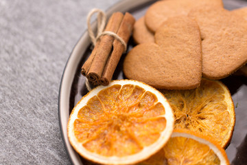 drinks and season concept - plate with heart shaped gingerbread cookies, dried oranges, cinnamon and anise on warm blanket
