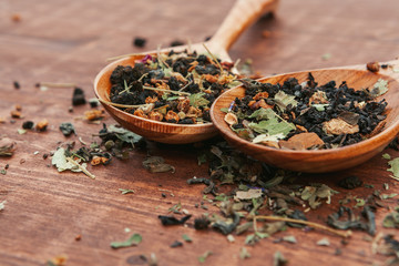 Black tea with herbs in wooden spoons on a wooden board